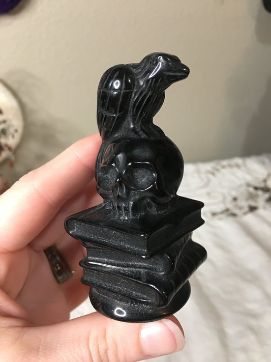 black obsidian raven, skull, and book stack